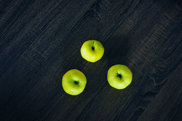 Green apples on a dark table.
Three sweet fruits viewed from above on a dark painted wooden table. Wallpaper with natural products and fruits. Color contrast and minimalism.