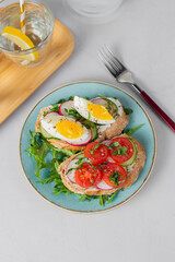 Toasted sandwiches white bread with cream cheese, vegetables: cherry tomatoes, cucumbers, eggs, parsley. Healthy vegetarian breakfast idea. Served with fresh lemon water, light background