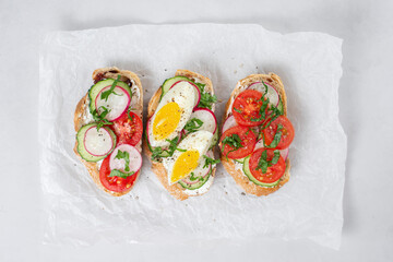 Delicious toasted sandwiches white bread with cream cheese, vegetables: cherry tomatoes, cucumbers, eggs, parsley. Healthy vegetarian breakfast idea. Served on craft paper, light background