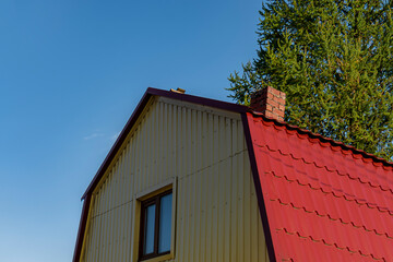 Attic red roof is made of metal from the house with a window. Outdoors of day. Back view.