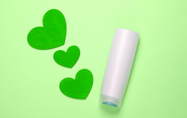 Shampoo bottle with hearts on green pastel background. Beauty care. Top view. Minimalism