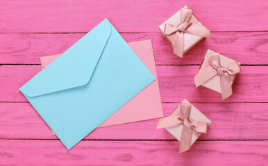 Envelope with gift boxes on pink wooden background. Top view