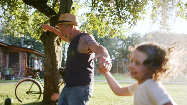 Family having a garden party, grandfather running through stream of water with kids.