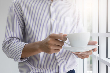 young man standing by the window with a coffee cup at his house in the morning prepares to go to work. Businessman stand to eat coffee in a relaxed mood in the office.