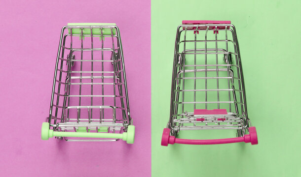 Two mini supermarket trolleys on blue pink pastel background. Shopping concept. Top view. Minimalism