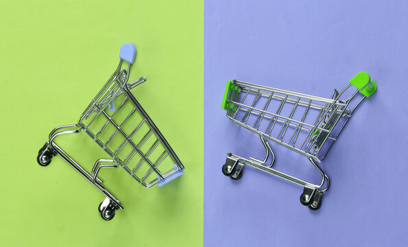 Two mini supermarket trolleys on blue pink pastel background. Shopping concept. Top view. Minimalism