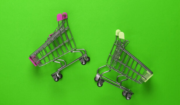 Two mini supermarket trolleys on green background. Shopping concept. Top view. Minimalism