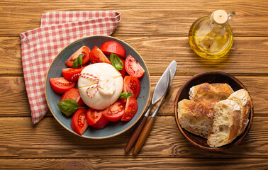 Italian salad with fresh tomatoes, burrata cheese, basil served on ceramic plate with ciabatta...