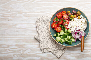 Greek mediterranean salad with tomatoes, feta cheese, cucumber, whole olives and red onion in blue ceramic plate on white wooden background from above, traditional appetizer of Greece with copy space