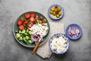 Greek mediterranean salad with tomatoes, feta cheese, cucumber, whole olives and red onion in blue ceramic plate on gray concrete background from above, traditional appetizer of Greece