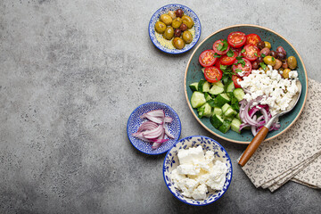 Obraz na płótnie Canvas Greek mediterranean salad with tomatoes, feta cheese, cucumber, whole olives and red onion in blue ceramic plate on gray concrete background from above, traditional appetizer of Greece with copy space