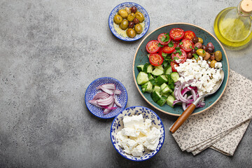 Fototapeta na wymiar Greek mediterranean salad with tomatoes, feta cheese, cucumber, whole olives and red onion in blue ceramic plate on gray concrete background from above, traditional appetizer of Greece with copy space