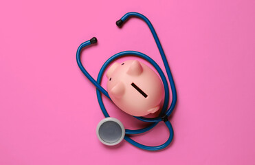 Medicine still life. Piggy bank with stethoscope on pink background. Top view