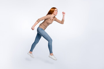 Full length photo of charming hurrying ginger lady wear beige shirt smiling jumping high running isolated white color background