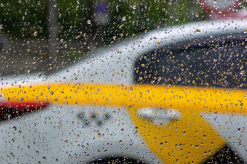 the silhouette of a yellow taxi through the glass in the raindrops