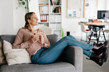 Trendy young woman in black leather boots relaxing on a sofa