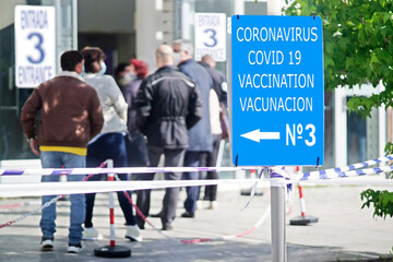 people queue draggle with coronavirus mask to get the covid vaccine ,  focus in  signage in english...