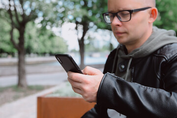 
Male hand with a smart phone close-up. Young caucasian man holds black mobile phone in his hand and looks at  screen, writes message or reads news. Selective focus.