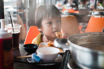 Little Asian toddler boy tries to eat crispy fried food at restaurant