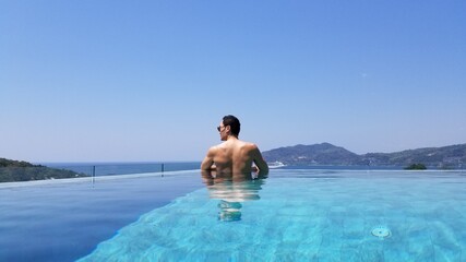 Muscular asian man relaxing in an infinity pool oceanside in a luxery resort sunbaking