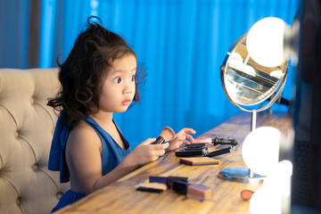 Adorable happy Asian little girl trying and checking makeup in front of the mirror in dressing room