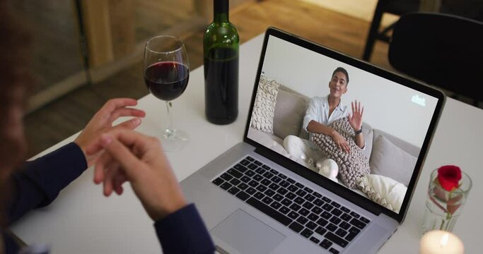 Mixed race man sitting at table using laptop making video call with male friend
