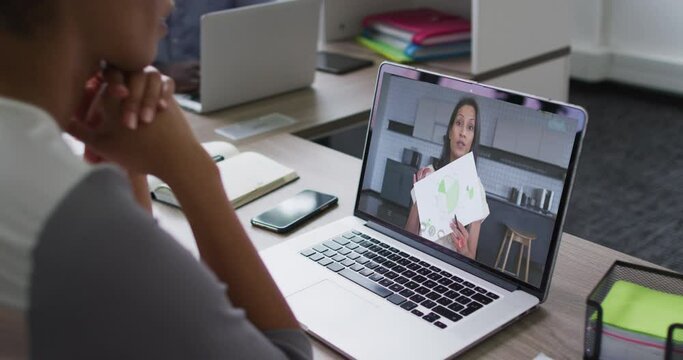African american businesswoman sitting at desk using laptop having video call with female colleague
