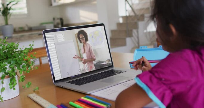 African american girl doing homework while having a video call with female teacher on laptop at home