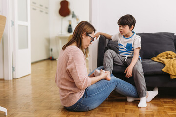 mother helps her son to puts on socks