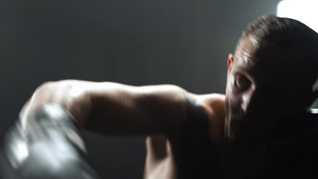 Boxer ferociously punching a boxing bag during his training,dark gym.