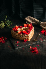 Confectionery concept - red and white cake in heart shape for St. Valentine's Day on black table (plate). Sweet and romantic present - Strawberry Cake on dark black background.