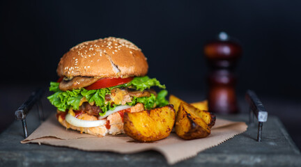 Tasty grilled homemade beef burger, tomato, cheese, cucumber and lettuce with french fries on a wooden background. Burger on the board on a dark background.