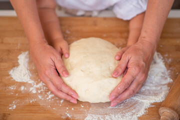 Mother and child hands prepares the dough with flour on rustic wooden table from above. Homemade pastry for bread or pizza. Bakery background.