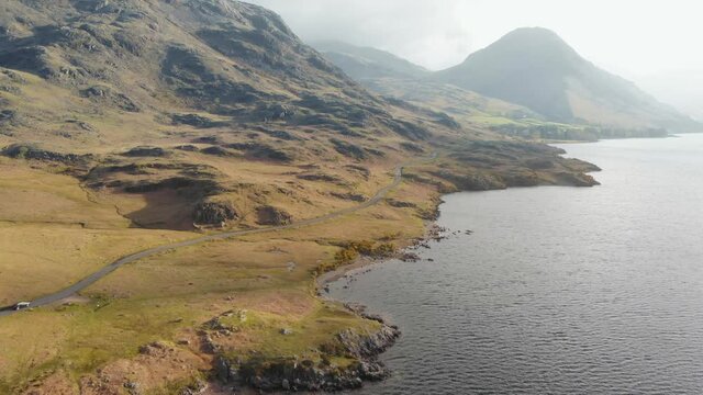 Aerial shot of single car driving along scenic lakeside highway, Lake District National Park