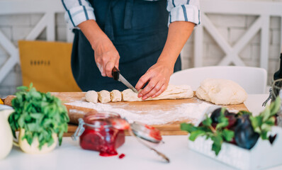 Cook hands kneading dough, piece of dough with white wheat flour. Cooks roll the dough for baking, pieces of raw dough on the wooden board.