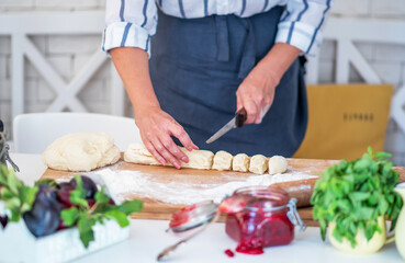 Cook hands kneading dough, piece of dough with white wheat flour. Cooks roll the dough for baking, pieces of raw dough on the wooden board.