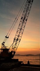 Large loading Crane by the seaside harbour at sunset with a lonely man sitting next to it isolated, finishing work shot at Sai Wan Shek Tong Tsui area Hong Kong Island
