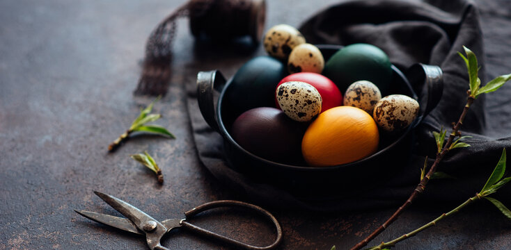 Vintage iron tray full of colorful Easter eggs with hay and spring branch on a dark rustic background. Copy space.