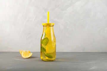 Refreshing summer drink with lemon, honey and mint. Yellow transparent glass bottle on grey background.  Space for your text