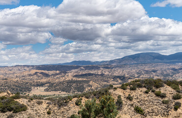 Fototapeta premium Los Padres National Forest, CA, USA - May 21, 2021: Heavy blue cloudscape over park east side wide scenery. Beige brown naked rocks and green shrub sprinkled all over.