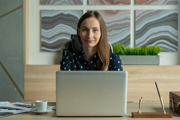 Fototapeta premium Portrait of a young woman in a shirt, working on a laptop in the office and looking at the camera