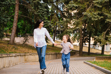 Obraz premium A little girl with her mother runs along the sidewalk in the park. Active play in nature.