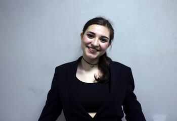 Smiling girl in a black jacket on a light background. Beautiful young girl in a formal suit