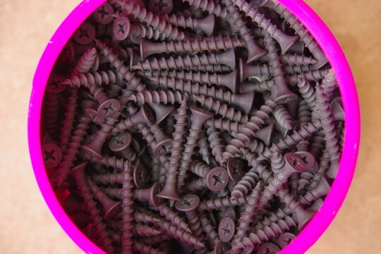 Toma cenital de un tarro de pl&aacute;stico de color morado, repleto de tornillos negros del tipo utilizado para la fijaci&oacute;n de placas de pladur.