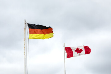 A German and Canadian flag flying side by side on a cloudy sky