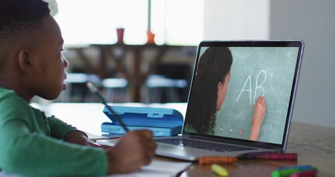 African american boy doing homework while having a video call with female teacher on laptop at home