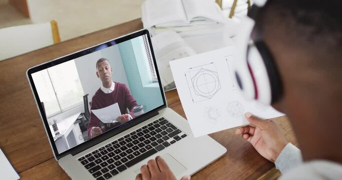 African american male college student holding notes while having a video call on laptop at home