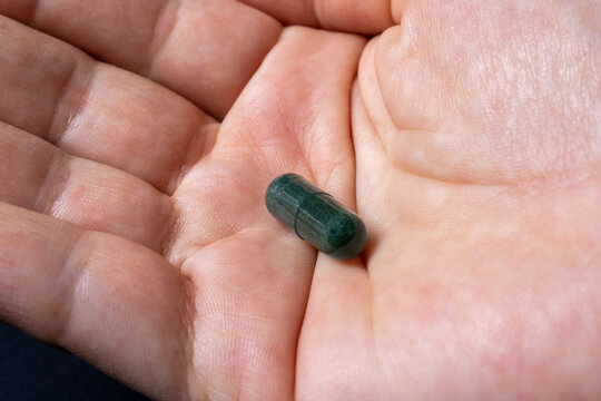 Spirulina capsule, lactose-free platensis and glutem on the hand of a white woman. a dietary supplement obtained from cyanobacteria, a class of single-celled organisms formerly known as blue algae.