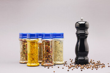 Different spices in jars and black pepper mill on gray background.