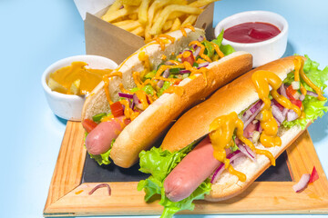 Barbecue grilled fastfood, Various traditional american hot dogs set with sausage, yellow mustard, ketchup and fresh vegetables salad, top view on bright blue background with french fries